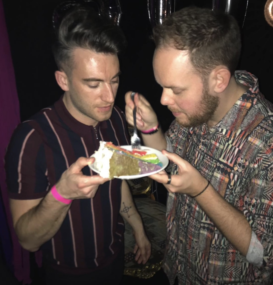 Two white men eating rainbow cake